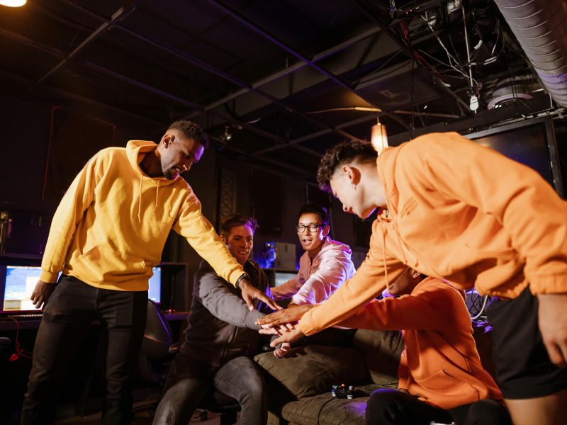 Group of diverse young gamers uniting in teamwork in a gaming room, celebrating victory.