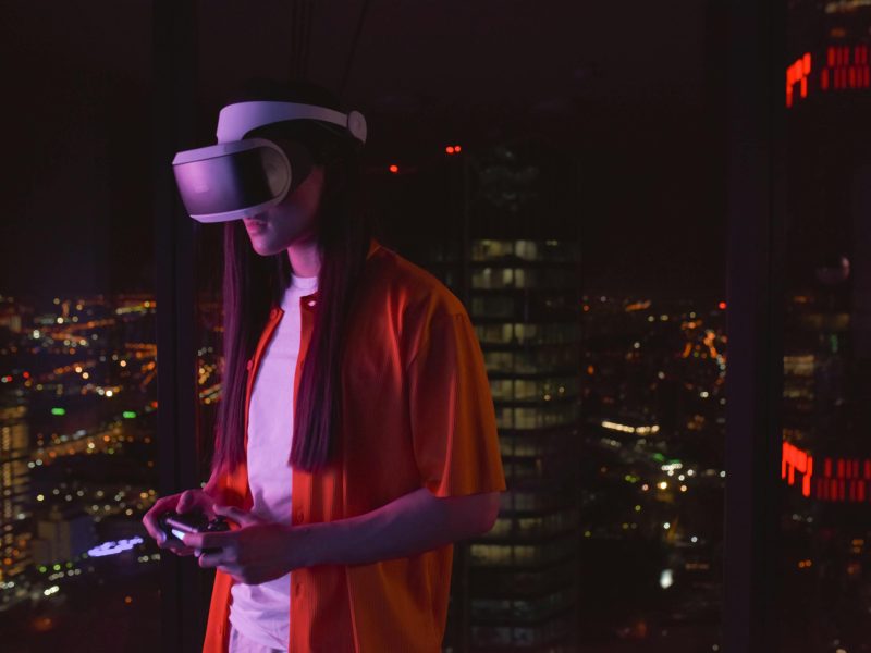 Young adult wearing a VR headset playing in an urban high-rise at night.