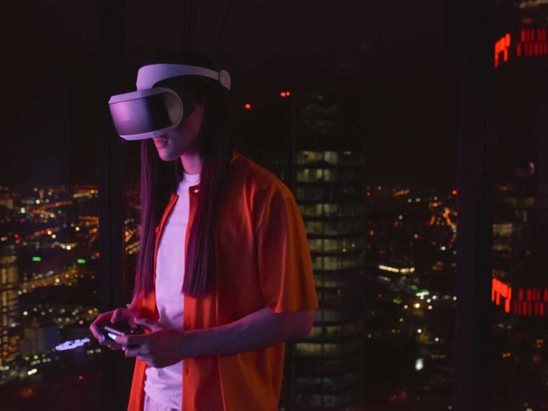 Young adult wearing a VR headset playing in an urban high-rise at night.